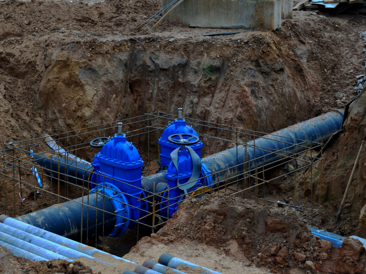 blue water main pipe in the ground with a blue valve surrounded by dirt